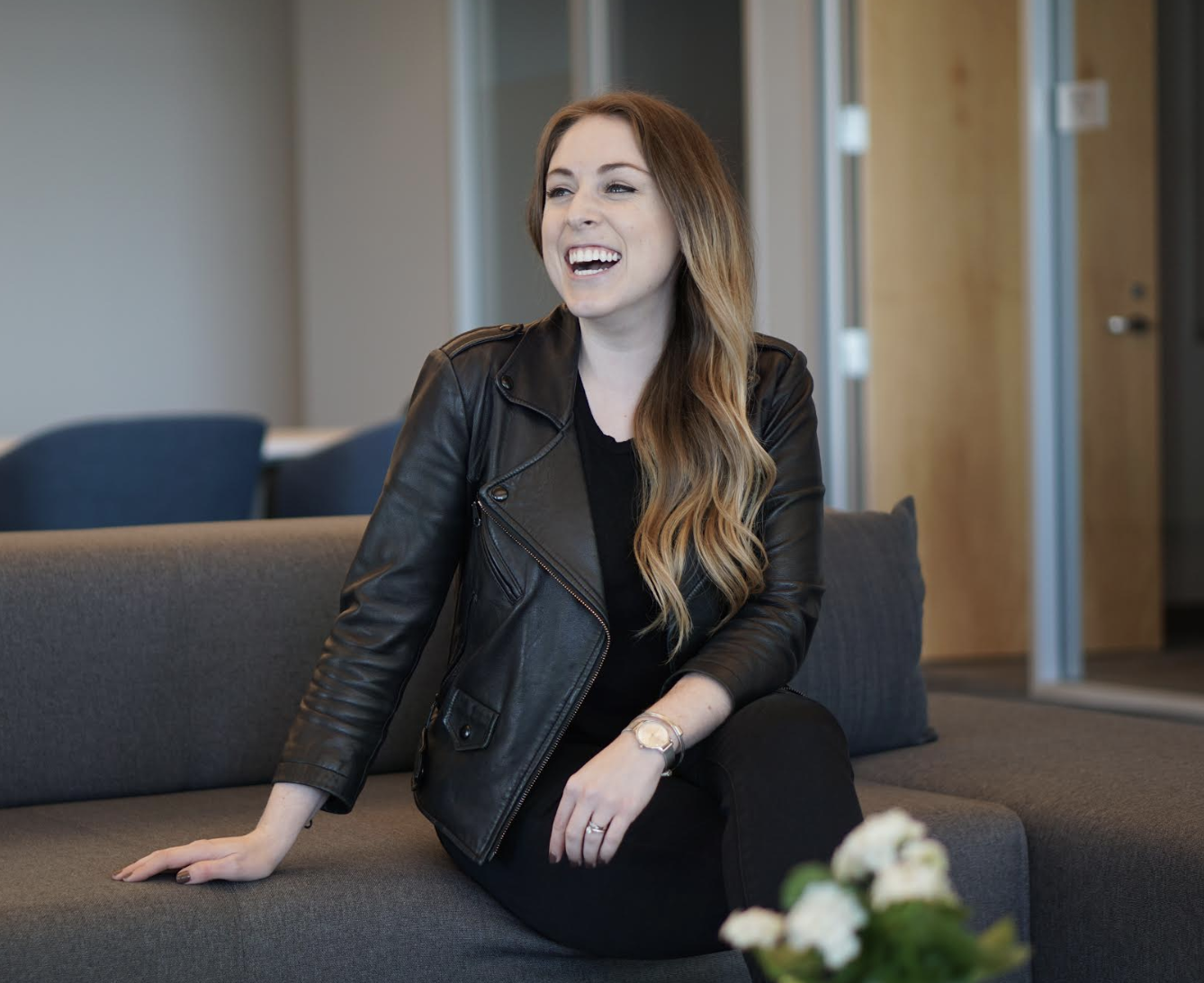 Rachel Tobac, Social Engineer sits on grey couch in office building, laughing